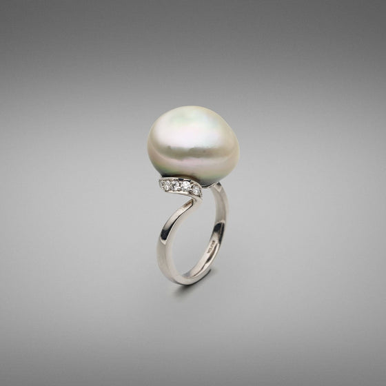 A BUNDA 'Lyra' Cultured Tahitian Pearl and Diamond ring made in 18 carat white gold, set with a button shaped pearl of clean skin and excellent lustre, platinum in colour with green tones. Round brilliant diamonds are thread-set in ribbon style setting beneath the pearl swirling to a plain shank in 18ct white gold.  Dimensions of pearl: 15.40mm  Weight of diamonds: 20 =0.38ct, F Colour, VS Clarity  Total weight of Ring: 9.46g