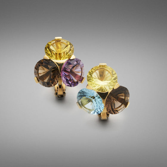 A pair of BUNDA 'Krest' multi gemstone earrings in 18ct yellow gold. One earring is set with lemon quartz, blue topaz and smoky quartz; while the other earring is set with lemon quartz, amethyst and smoky quartz; all in 18ct yellow gold 'Krest' claw settings. Each earring is fitted with a post and a large Omega clip.