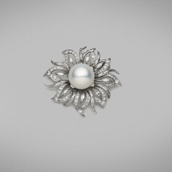 A BUNDA Australian Cultured South Sea pearl and diamond brooch made in 18ct white gold, set with a button shaped pearl of clean skin and excellent lustre, white in colour with strong pink tones. The brooch is set with round brilliant, baguette and marquise cut diamonds in a fanciful flower design.  Dimensions of pearl: 14mm  Weight of diamonds: 3.62ct  Total weight of Brooch: 24.4g