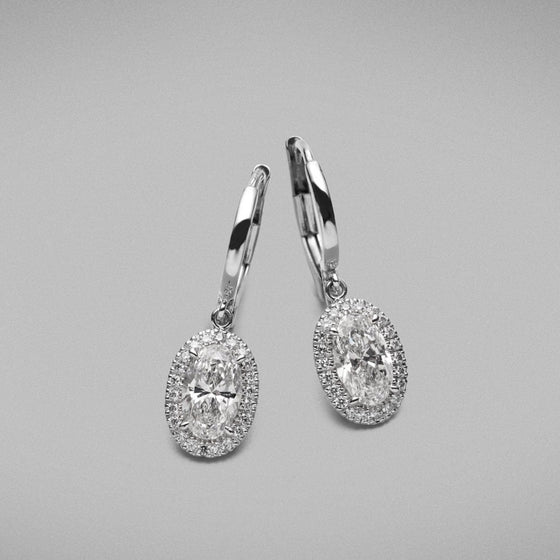 A pair of BUNDA 'Mignon' Diamond Drop Earrings in platinum. Each earring is set with an oval brilliant cut diamond with micro castle set round brilliant diamonds to the head. Fittings are European curved post and clip.  Characteristics of Oval Cut Diamond; 0.7ct, G colour / SI2 Clarity. Characteristics of Oval Cut Diamond; 0.7ct, F colour / SI2 Clarity.  Characteristics of Additional Round Brilliant Cut Diamonds: 44 = .21ct, F colour, VS Clarity  Total weight: 3.66 grams.