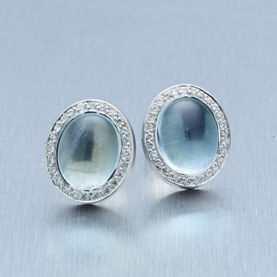 A pair of BUNDA 'Corvus' aquamarine earrings in 18 carat white gold, featuring a pair of cabochon cut aquamarines, bezel set and surrounded with threadset, round brilliant cut diamonds, fitted with a post and butterfly fitting.  Weight of aquamarine: 2 = 5.63ct.  Characteristics of diamonds: 52 = 0.23ct, F colour, VS clarity.